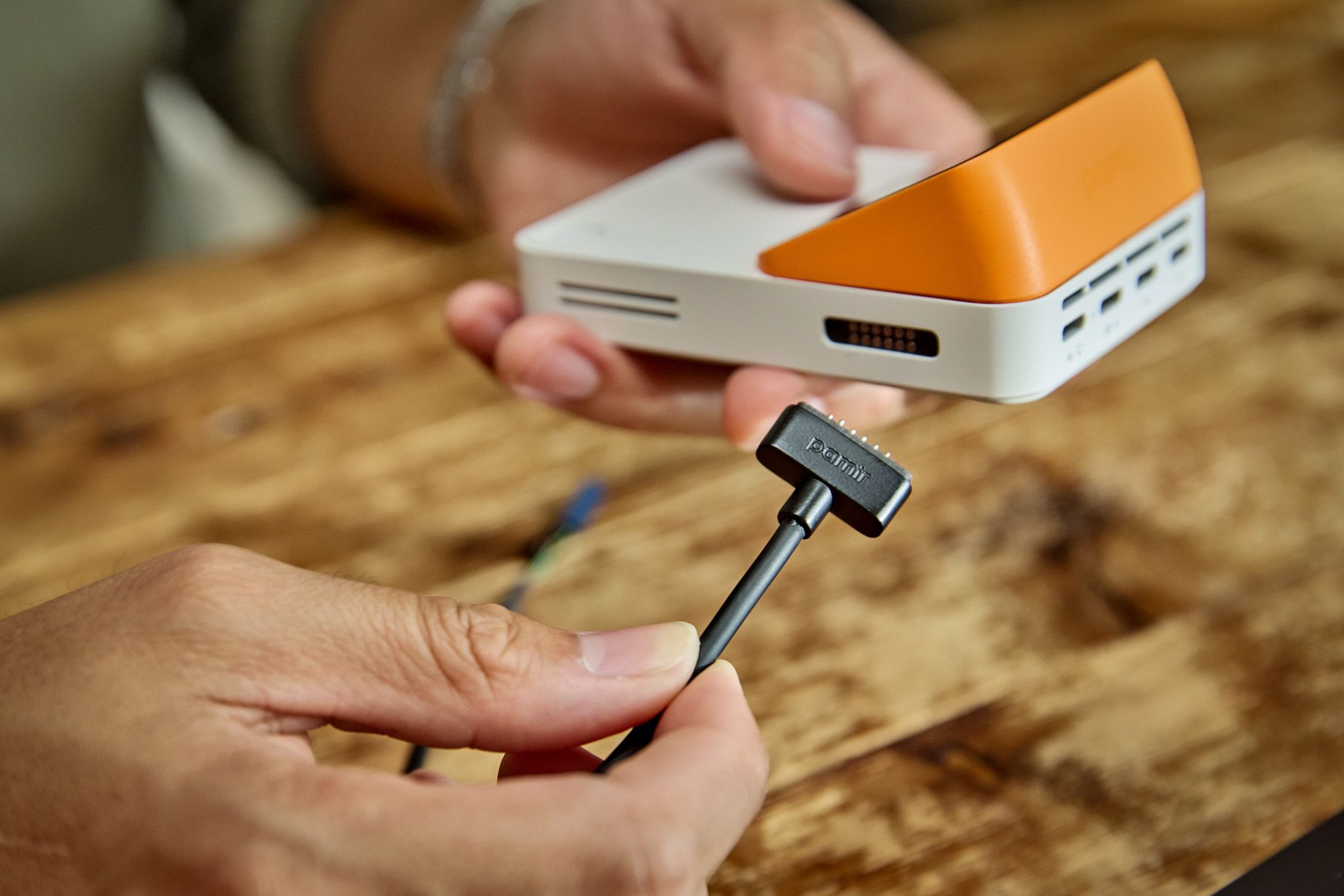 A person holding a Lapis One and its GPIO connector above a wooden workbench.